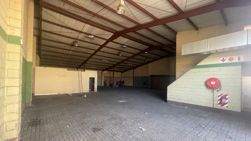 The warehouse interior before work, with a brick floor and exposed steel roof trusses.