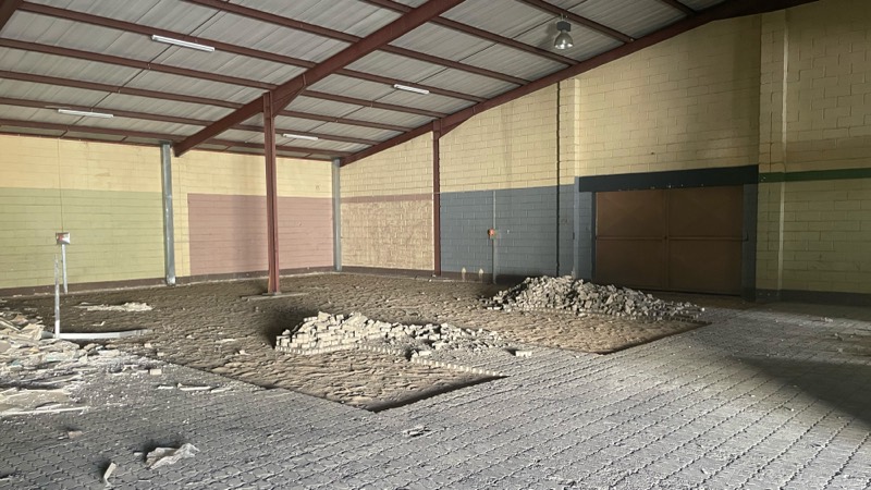 The warehouse interior with the concrete floor broken up and rubble piled in the middle.