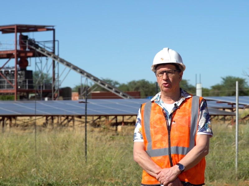 An interviewee in a hard hat and safety vest in front of the plant and solar array.
